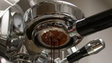 Kaffeemaschine brüht Espresso, Tropfen fallen in Tasse.