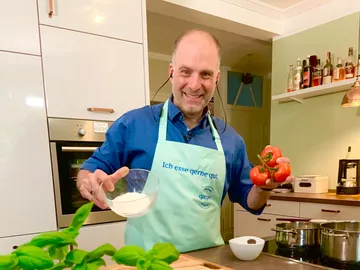 Man in kitchen apron holds tomatoes and flour bowl.