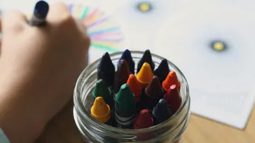 Colored pencils in a glass, someone is drawing with a pen.