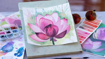 Watercolor drawing of a flower on a table with painting supplies.