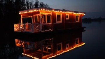 Schwimmendes Haus mit Lichtern reflektiert im ruhigen Wasser.