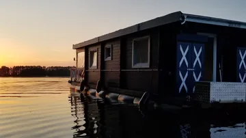 Hausboot schwimmt ruhig im Wasser bei Sonnenuntergang.