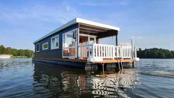 Houseboat swims calmly in water under blue skies.
