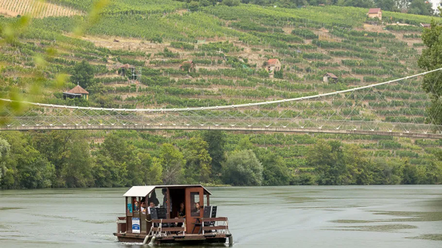 Ein Floß fährt auf einem ruhigen Fluss unter einer Hängebrücke.