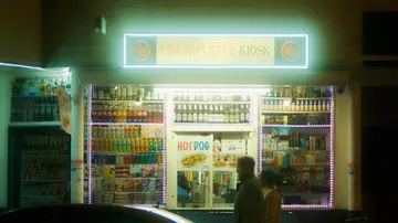 Kiosk verkauft Snacks und Getränke unter neonbeleuchtetem Schild.