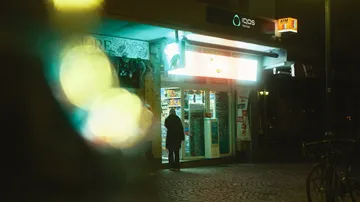 Ein Mann steht vor einem beleuchteten Kiosk in der Nacht.