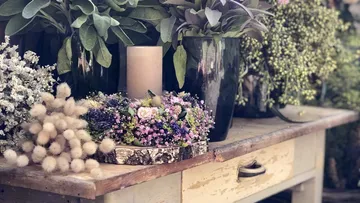 Flower arrangement on wooden plate next to candle and plants.