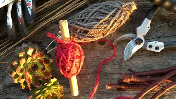 Wool and plants lie on a wooden table, tools next to them.