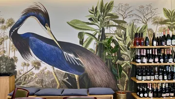 Blue heron on wall, next to wine rack with bottles.