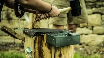 Holzblock, Hammer wird gehalten, im Freien mit Steinmauer.