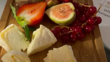 Cheese and fruit lie on a wooden board.