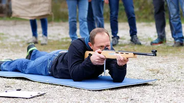 Mann liegt auf dem Boden und zielt mit Gewehr.