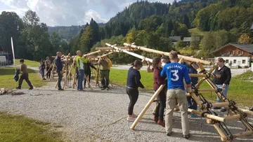 Gruppierung von Menschen baut eine Struktur aus Holzstangen.