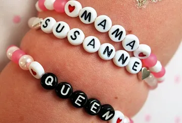 Bunte Armbänder mit Namen und Symbolen an einem Handgelenk.