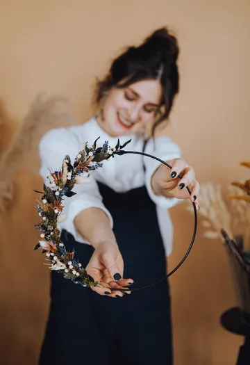 Woman presenting wreath against a large, bright background.