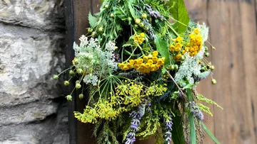Ein Gartenschmuck aus bunten Blumen hängt an Holz.
