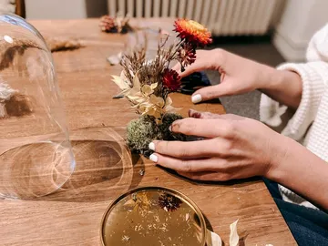 Hands arrange dried flowers on a table.