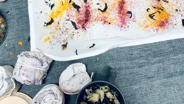 Colored pigments on a cloth surrounded by fabrics and shells.