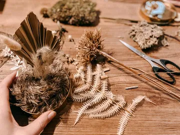 Hands create dried flowers on a table with tools.