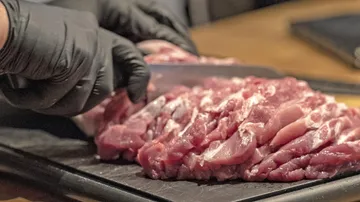 Fleisch wird mit einem Messer auf einem Schneidebrett geschnitten.