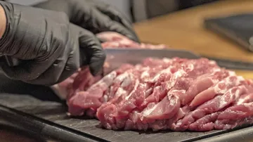 Meat is cut with a knife on a board.