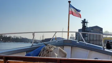 Boat with flag sails on calm water, sunny sky.