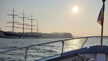 Boat sails on water, looking at a large sailing ship.