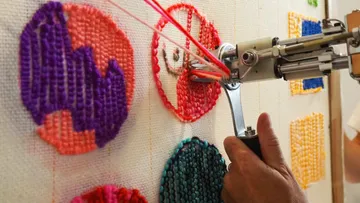Ein Roboter stickt bunte Muster auf einem Stoffhintergrund.