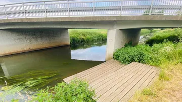 Brücke über einen ruhigen Fluss mit Holzsteg darunter.