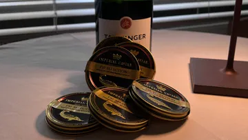 Caviar cans lie on a table next to a wine bottle.