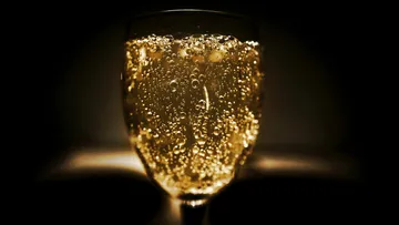 A glass of sparkling drink against a dark background.