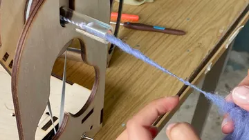 Woolen thread is processed with a spinning wheel, mounted on a table.