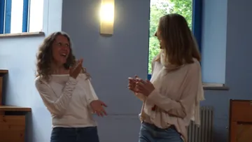 Two women laugh and interact in a bright room.