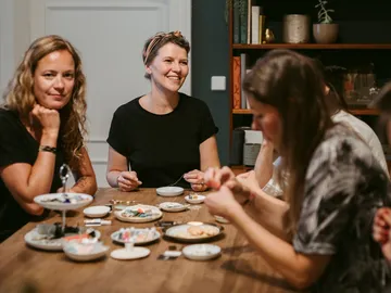 Women sit at a table and do crafts together.