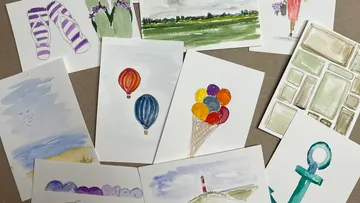 Colourful watercolor paintings lie on a table.
