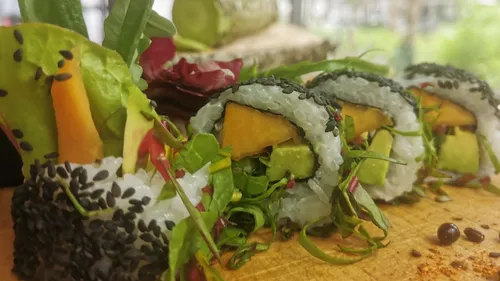 Sushirollen liegen auf einem Holzbrett, umgeben von Gemüse.