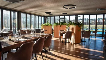 Bright restaurant atmosphere with plants and long wooden tables.