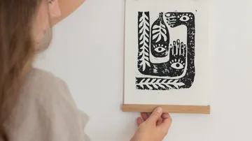 Frau hängt Druckkunst an die Wand in hellem Raum.