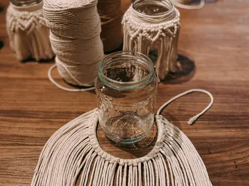 Glasgefäß liegt auf einem Holztablett mit Makramee.