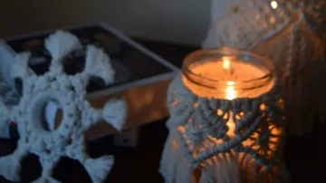 White macrame decoration and burning candle on table
