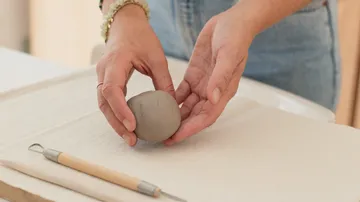 Hände formen einen grauen Knetball auf einem Tisch.