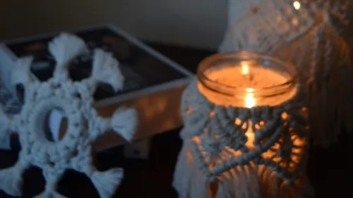 Candle glows in a handmade holder on a table.