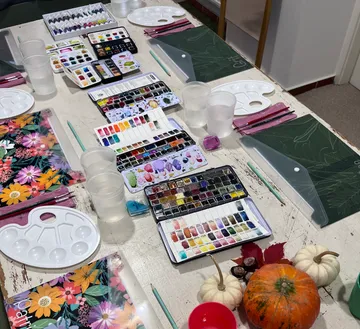 Maltische mit Farben, Wasserbehältern und verschiedenen Malutensilien.