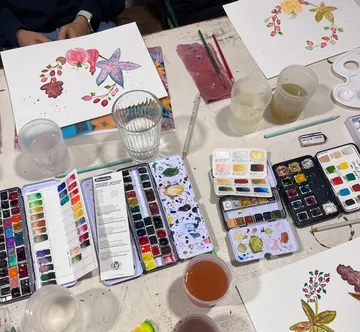 Aquarellfarben, Pinsel und Blumenillustrationen auf Tisch.
