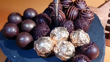 Dark chocolates lie on a round, black plate.