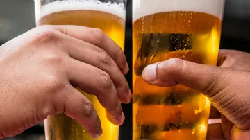 Zwei Hände stoßen Gläser mit Bier an.