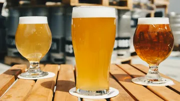Drei Biergläser stehen auf einem Holztablett im Freien.