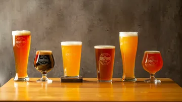Six glasses of different types of beer are on a table.