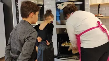 Kinder beobachten eine Frau, die Kekse aus dem Ofen holt.