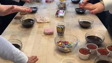 Bowls of ingredients stand on a table, hands move.